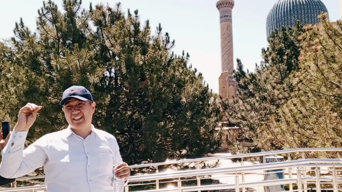 Tour guide briefing visitors near Gur-e-Amir in Samarkand, with the minaret and blue dome behind the trees